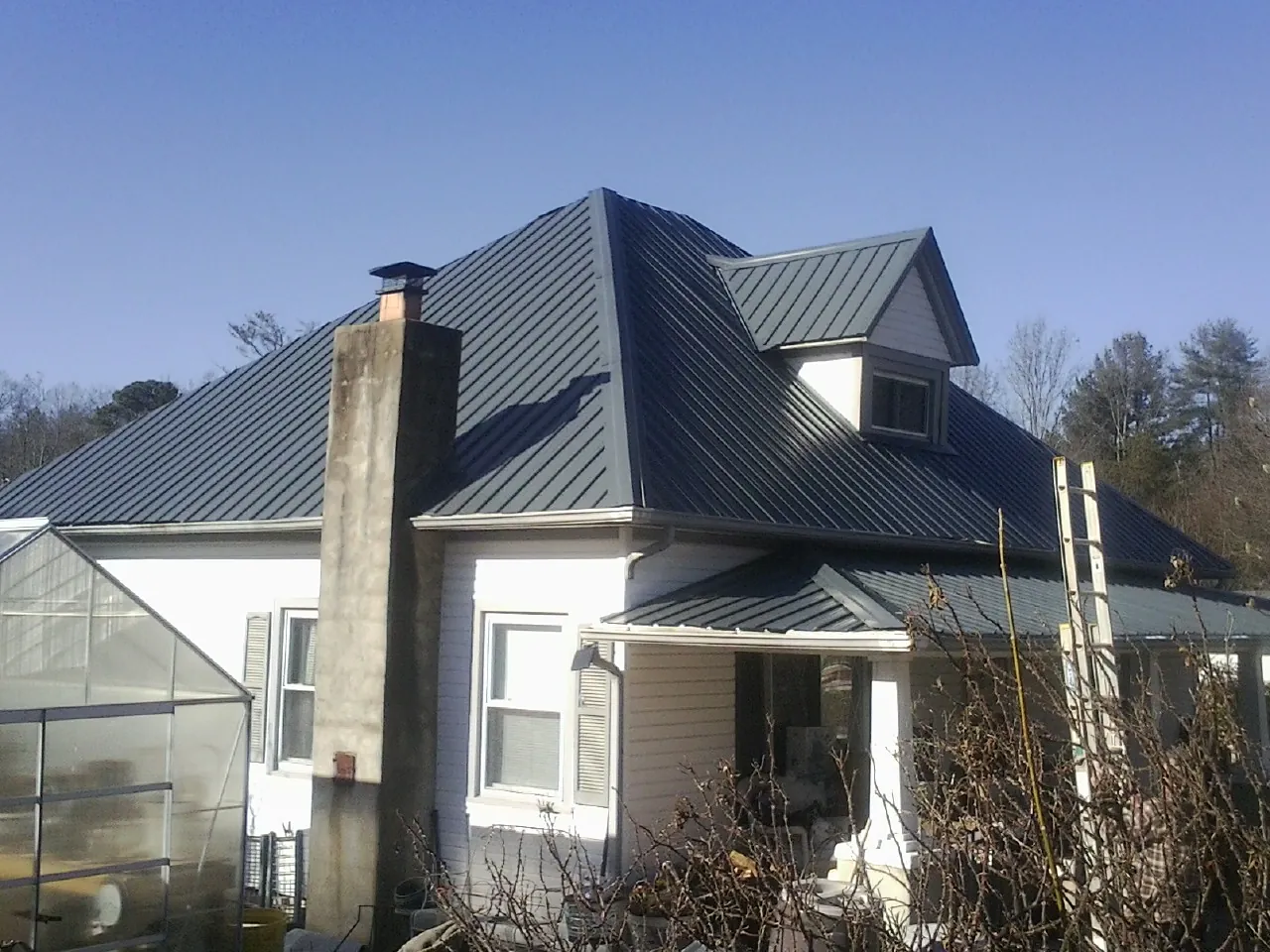 Dark blue standing seam metal roof on a white farmhouse with dormer — Slate & Tile Roof Repair by Roofing Brothers in Pine Island