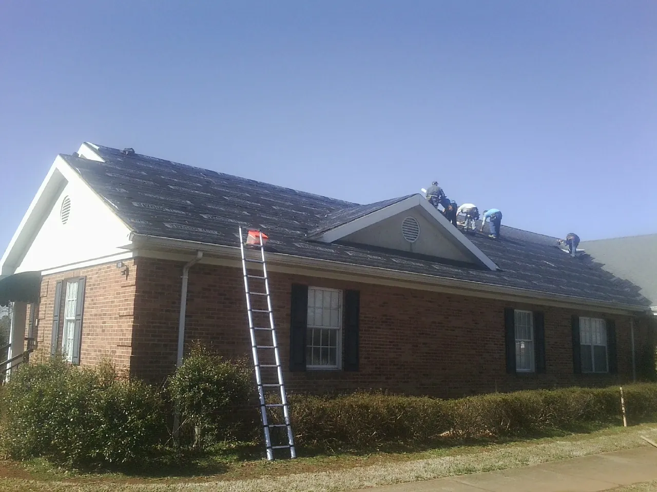 Crew tearing shingles off a brick ranch roof with a ladder set — Metal Roof Repair work by our crew in Pine Island