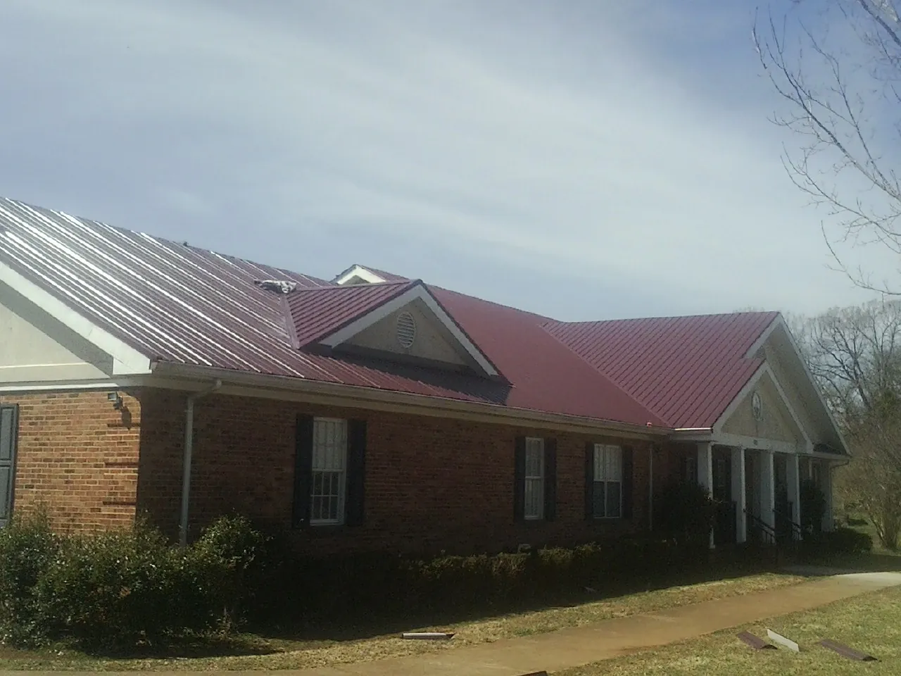 Red metal roof with gabled entries on a long brick building, from a Hail Damage Roof Repair job in Pine Island