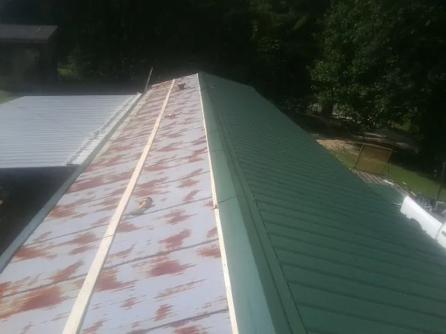 Old rusted panels beside newly installed green metal roofing — Wind Damage Roof Repair by Roofing Brothers in Pine Island
