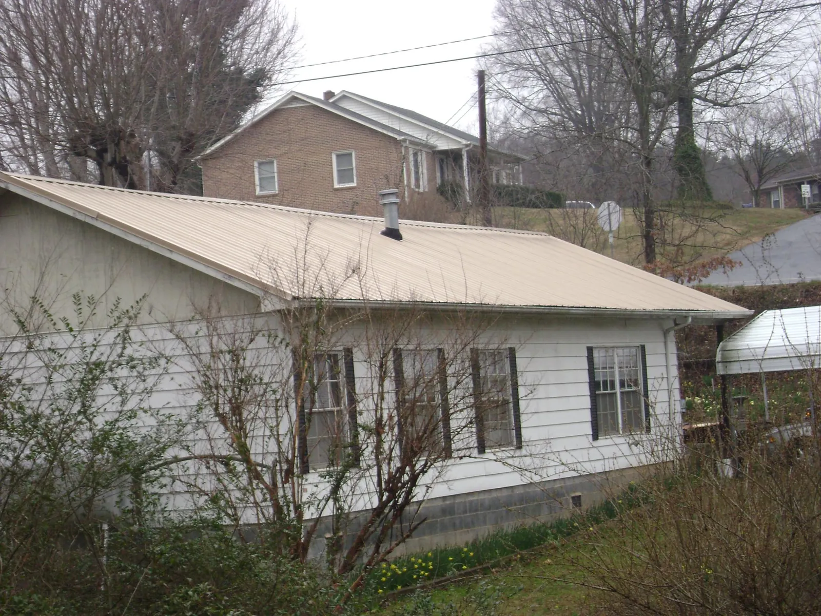Tan metal roof on a white sided house set into a hillside — Commercial Roofing by Roofing Brothers in Pine Island